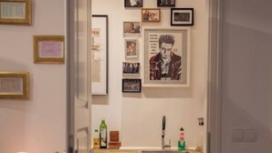 A narrow hallway leading to a kitchen with a sink, countertop, and framed pictures on the wall.