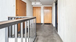 Un couloir avec des portes en bois numérotées de 19 à 21, une rambarde en métal et un sol en béton.