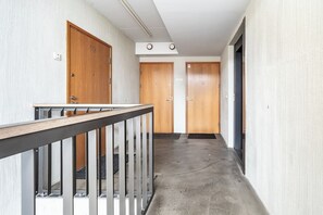 Een gang met houten deuren genummerd 19 tot en met 21, een metalen leuning en een betonnen vloer.