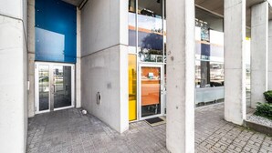 Un bâtiment doté d’une façade en béton, de grandes fenêtres en verre et d’un espace d’entrée pavé.