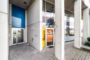 Een gebouw met een betonnen gevel, grote glasramen en een verhard entreegebied.