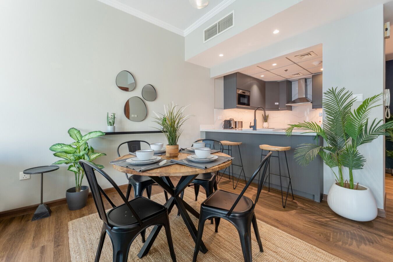 A modern kitchen with a central island, a dining area with a round table and chairs, and potted plants.