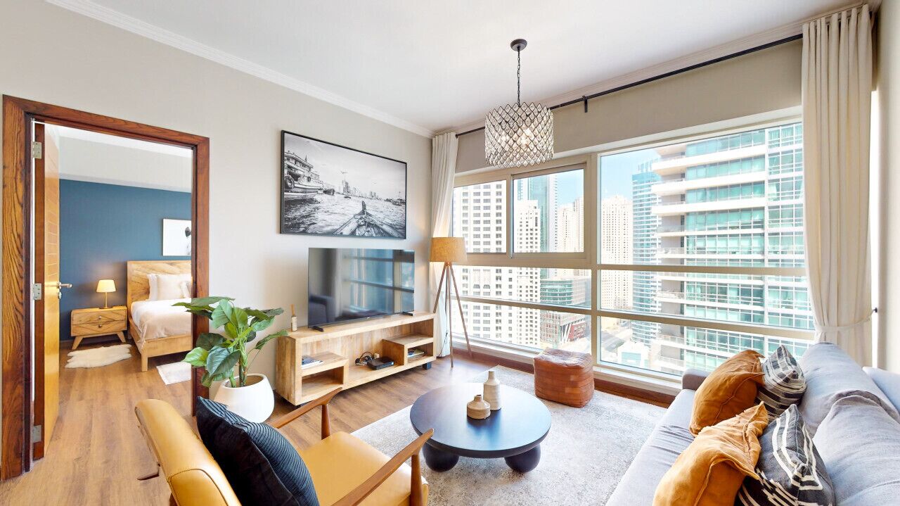 Una sala de estar moderna con sofá, mesa de centro, televisor y ventanas amplias que dan a vistas de la ciudad.