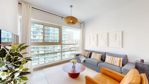 A modern living room with a large window, a grey sofa, a round coffee table, and a plant.