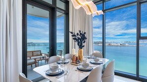 Een eetruimte met een tafel voor vier personen, grote ramen en uitzicht op zee.