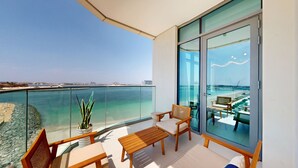 Een balkon met vrij uitzicht op zee, een houten tafel, twee stoelen en een bloempot.