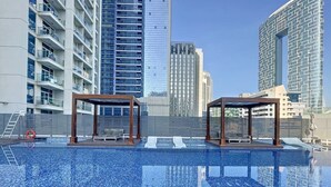 A swimming pool with two wooden gazebos, surrounded by high-rise buildings. - Cosy Studio l Aesthetic Finishes l Prime Location (Dubai Marina)