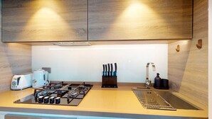A modern kitchen with a gas stove, two white toasters, a knife block, and a sink. - Cosy Studio l Aesthetic Finishes l Prime Location (Dubai Marina)