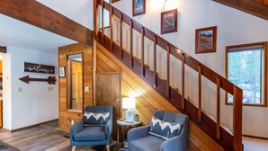 A wooden staircase with a railing, two armchairs with patterned cushions, a small table with a lamp, and a 'welcome' sign. - Hare 12 | Hot Tub | Dogs OK | Foosball + Darts | Bikes | 3BR/2BA (Sunriver)