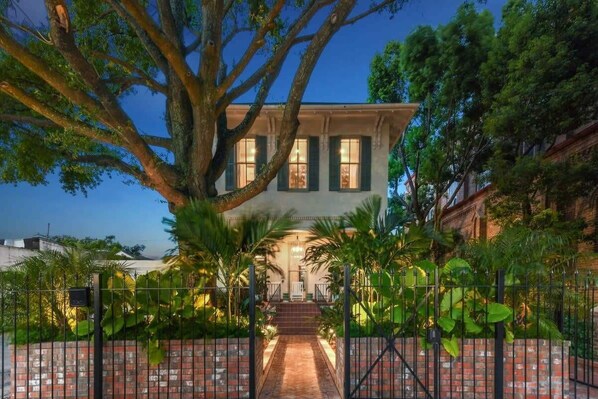 A large house with a brick pathway leading to the front door, surrounded by lush greenery and a black metal fence. - Grand 8BR NOLA Estate | Heated Pool & Spa (New Orleans)