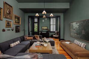 A living room with a sectional sofa, a coffee table, and a large painting on the wall. - Grand 8BR NOLA Estate | Heated Pool & Spa (New Orleans)