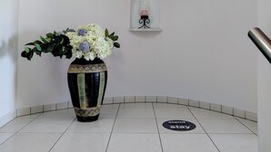 Een receptiegedeelte met een beveiligingscamera-bord, een potplant en een klein plankje met een decoratief object.