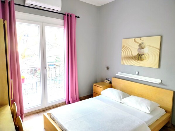Ein Hotelzimmer mit Bett, Nachttisch, Wandregal und einem Fenster mit Vorhängen.