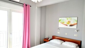 Een slaapkamer met een bed, een nachtkastje, een telefoon aan de muur en een raam met een roze gordijn.