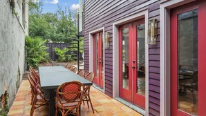 An outdoor patio with a dining table and chairs, surrounded by a purple building with red doors and windows.
