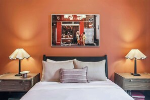 A hotel room with a bed, two bedside tables with lamps, a wall-mounted picture, and a red door. - Boutique 8BR B&B with Pool | Steps from French Q (New Orleans)
