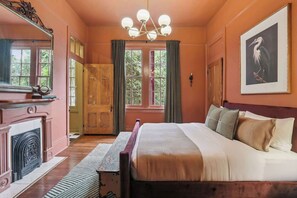 Ein Schlafzimmer mit einem großen Bett, einem Kamin, einer Kristallleuchter und einem fenster mit Vorhängen.