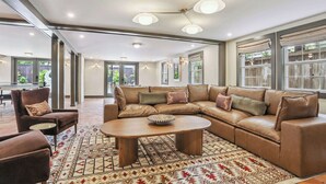 A spacious living room with a large leather sectional sofa, a round coffee table, and a patterned rug.