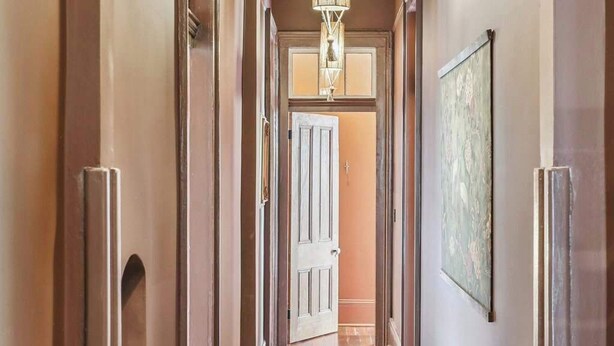 A hallway with wooden flooring, a chandelier, and a door at the end.