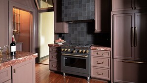 A kitchen with a dark brown tiled backsplash, a stainless steel range hood, and a built-in oven.