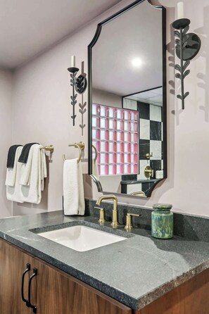 A bathroom with a large mirror, a sink with gold fixtures, and a vanity with a green container. - Boutique 8BR B&B with Pool | Steps from French Q (New Orleans)