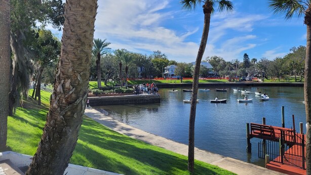 A serene park with a lake, boats, and palm trees.