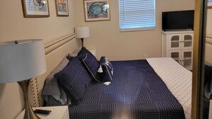 A bedroom with a bed, a nightstand, a lamp, a TV on a cabinet, and three framed pictures on the wall.
