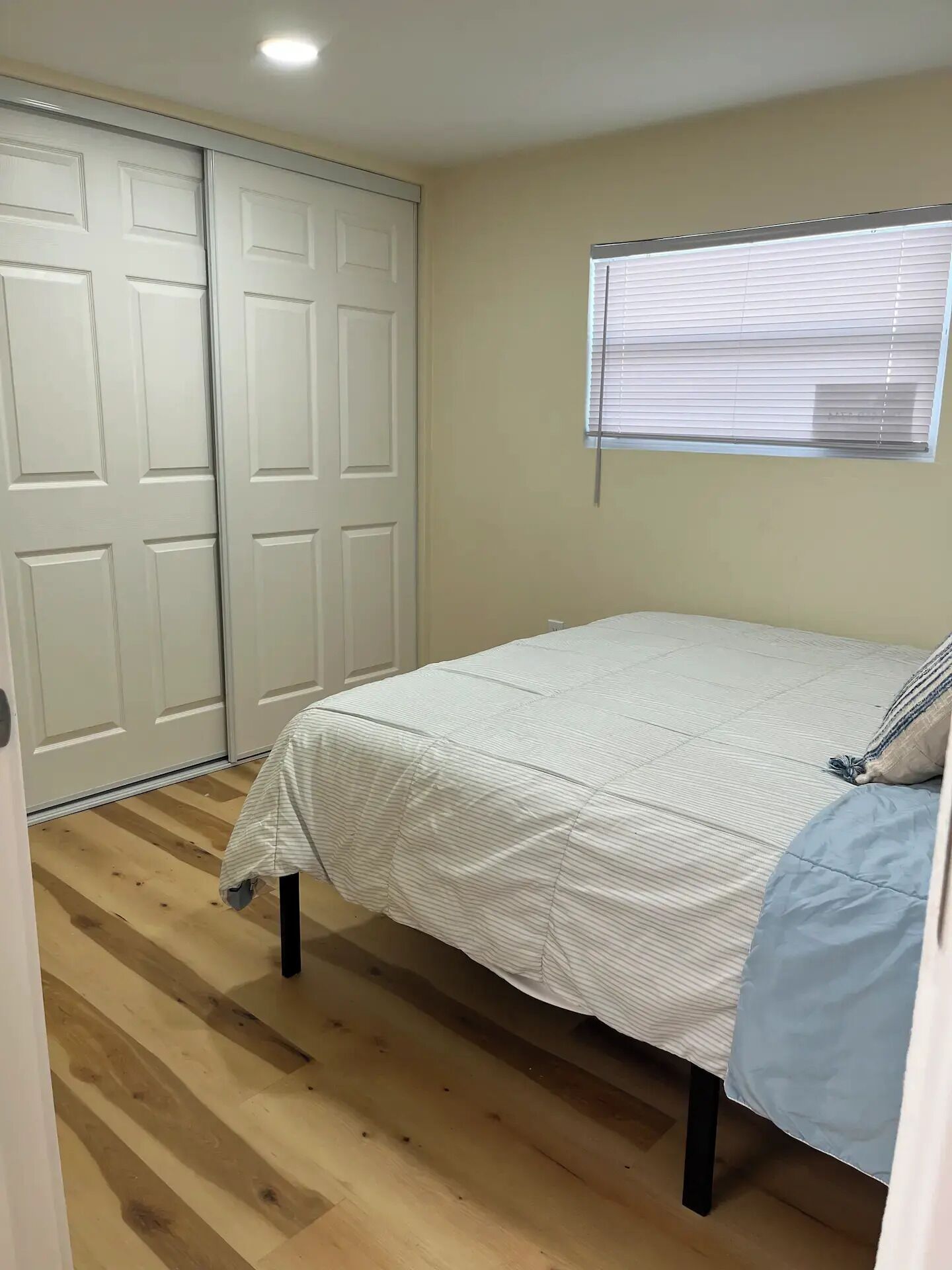 Une chambre à coucher avec un lit, un plancher en bois, une fenêtre avec des stores et un placard avec des portes coulissantes.