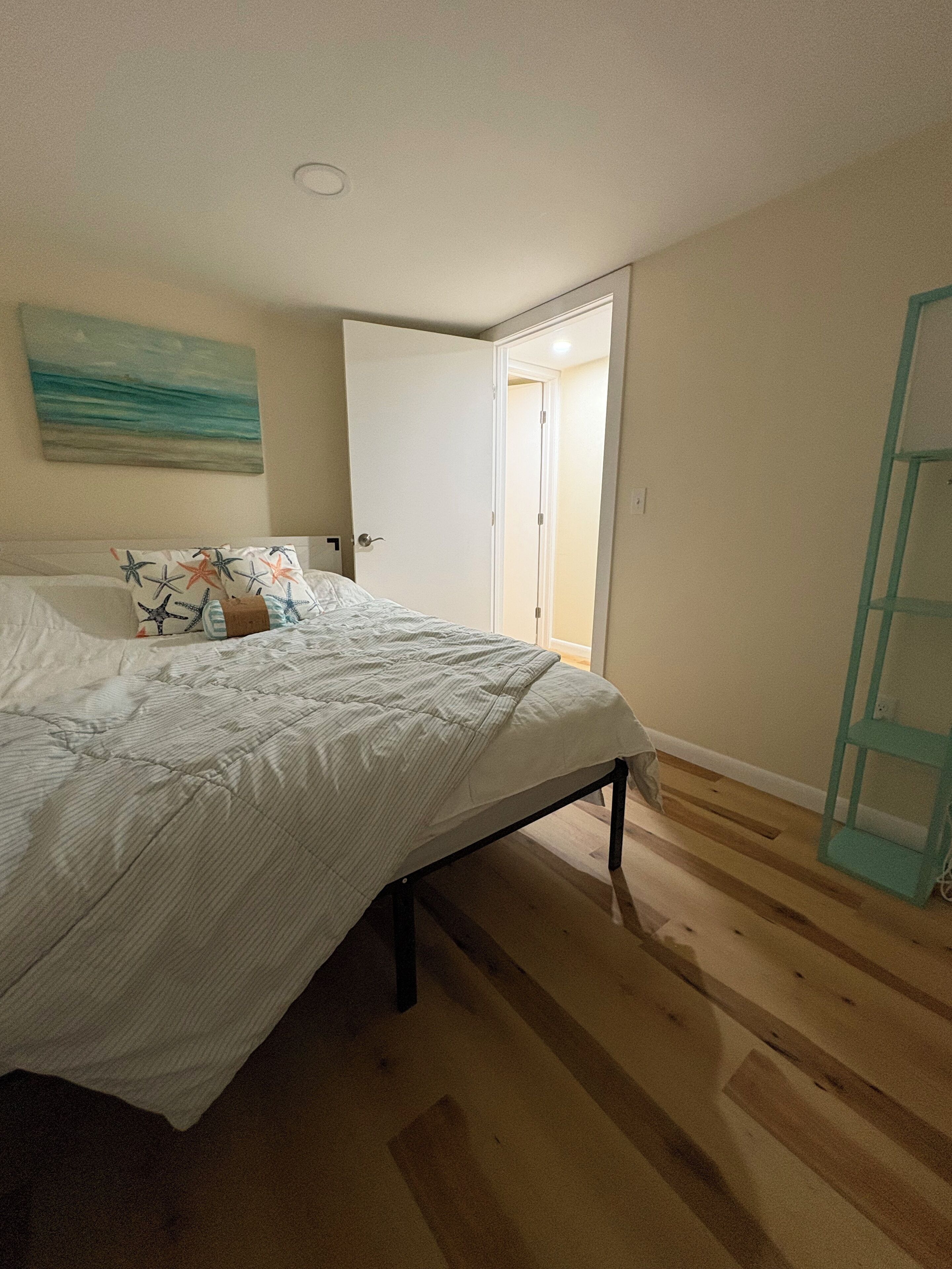 A bedroom with a bed, a door leading to another room, and a wooden floor.