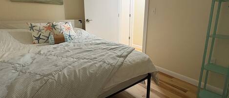 A bedroom with a bed, a door leading to another room, and a wooden floor.