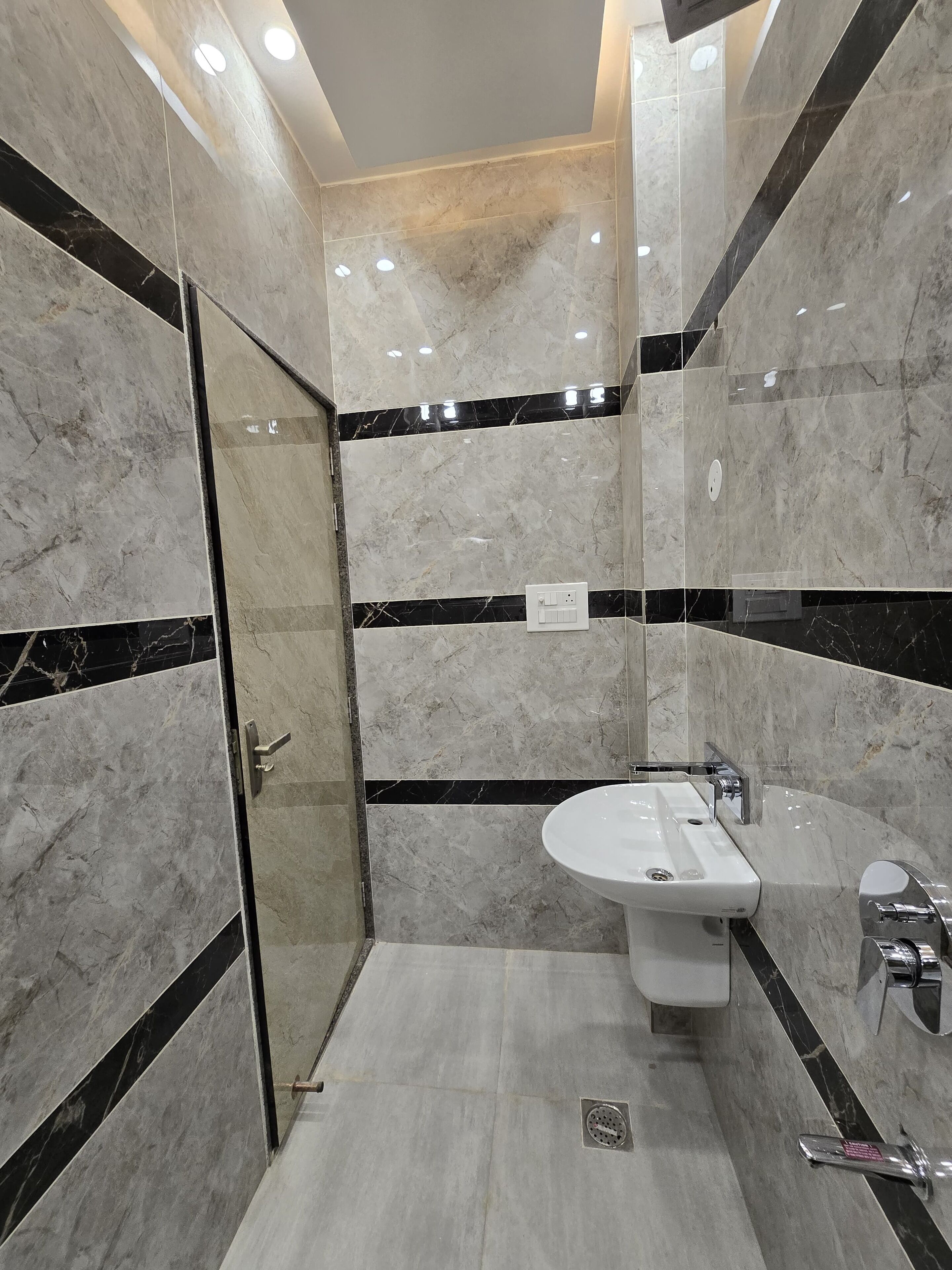 Un baño moderno con cabina de ducha de vidrio, lavamanos blanco y detalles en mármol negro.