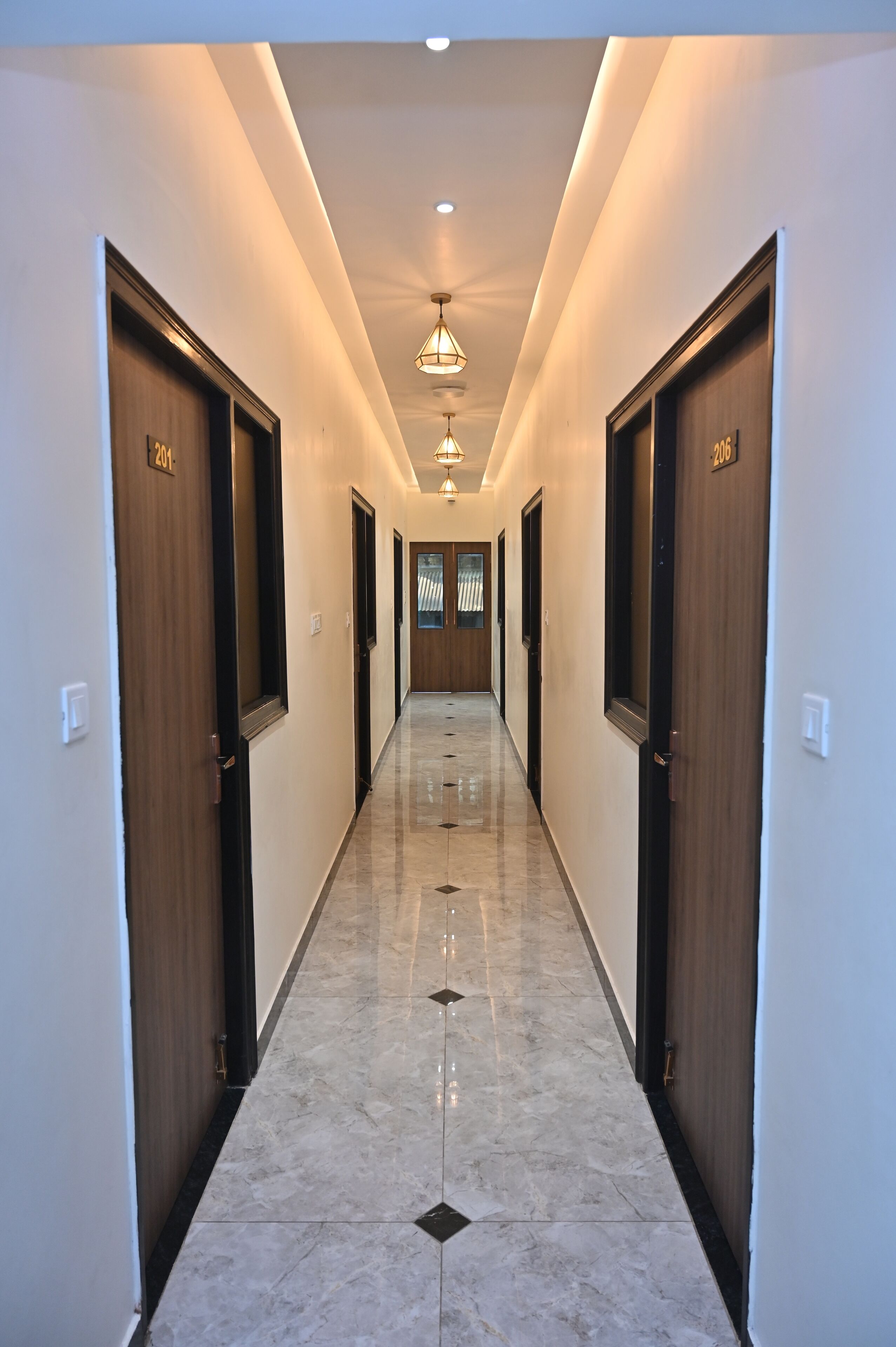 A hallway with wooden doors, marble flooring, and pendant lighting.