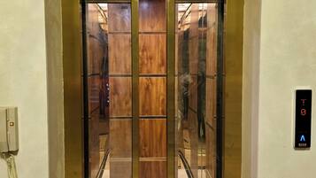 Un ascensor con acabado metálico, un cartel con la palabra 'LIFT' en la parte superior y un interruptor de incendios a la derecha.