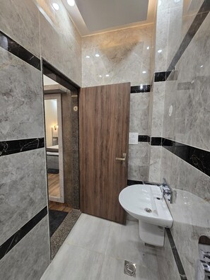 A modern bathroom with a marble floor, a wooden door, and a white sink. - Hotel Kashi Mantram (Varanasi)