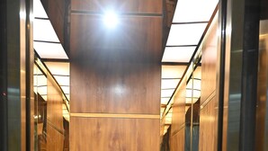 Ένας σύγχρονος σχεδιασμός για το εσωτερικό ενός ανελκυστήρα, με ανακλαστικές επιφάνειες στους τοίχους και ένα κεντρικό πάνελ από ξύλο.