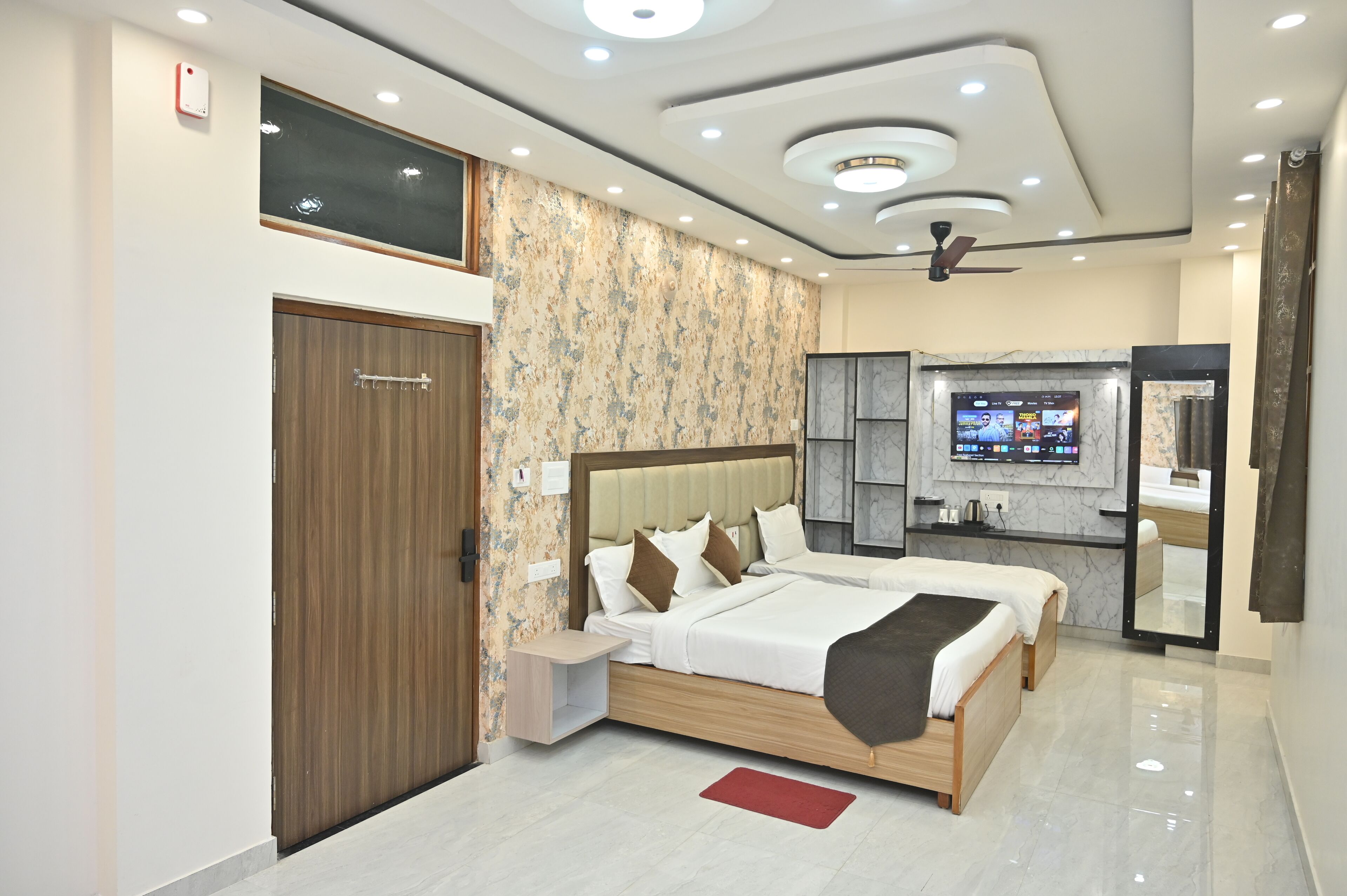 A modern hotel room with a large bed, a small bedside table, a mirror, and a TV mounted on the wall.