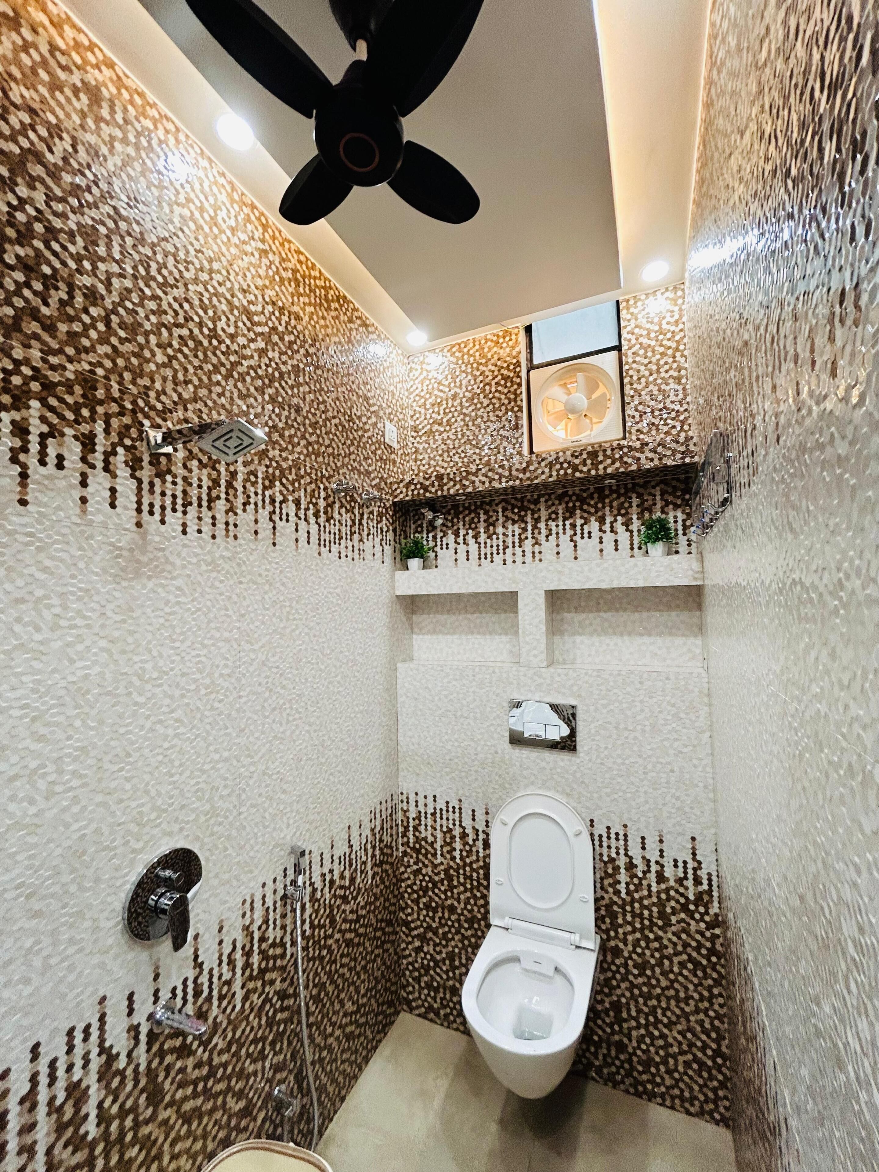 A bathroom with a patterned wall, a ceiling fan, a toilet, and a small shelf with a plant.