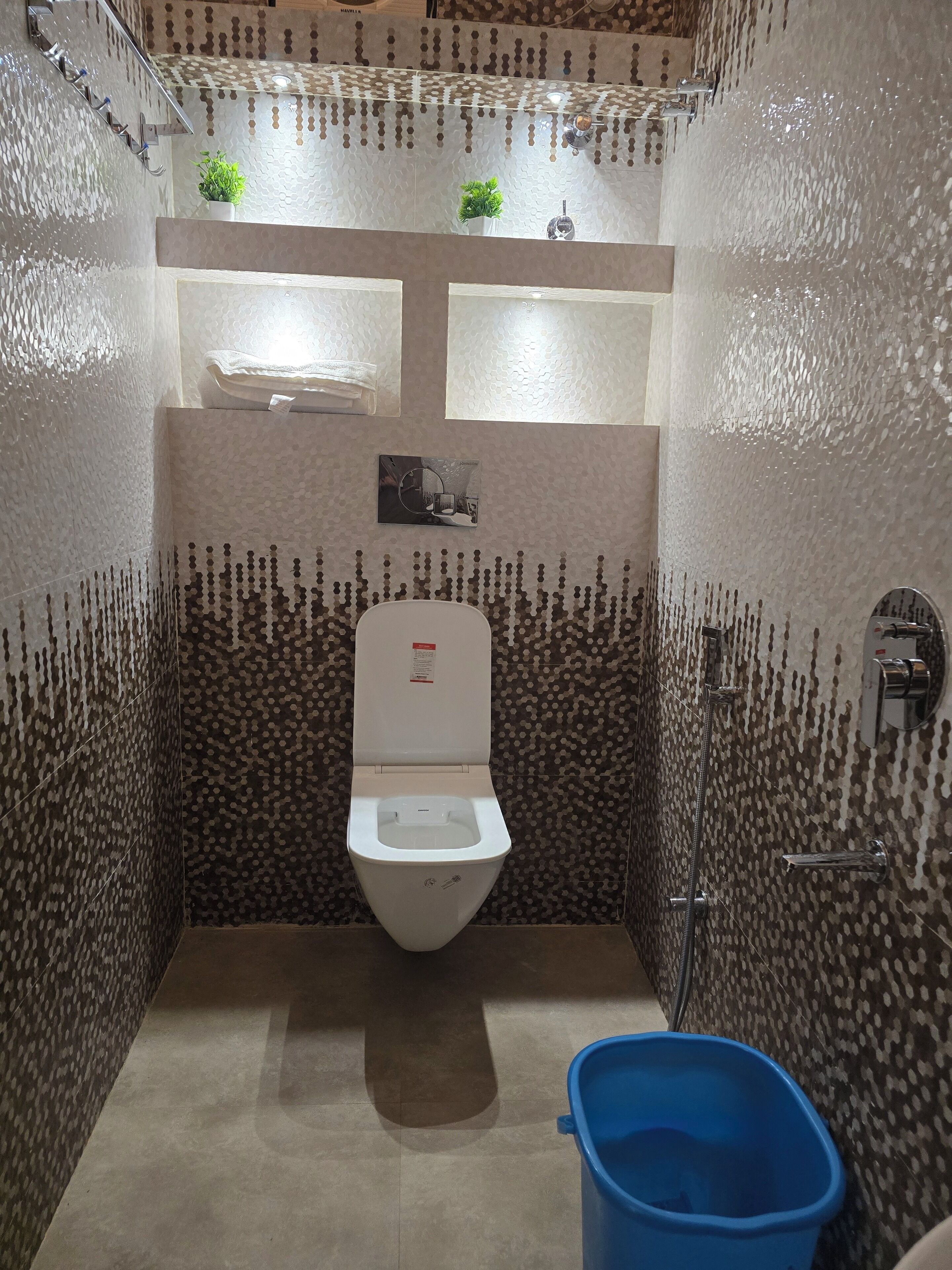 A small, compact bathroom with a toilet, a blue bucket, and a mirror.