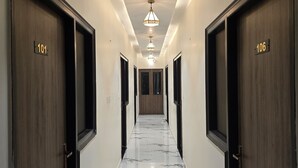 Ένας διάδρομος ξενοδοχείου με ξύλινες πόρτες με τους αριθμούς 101 και 106, μαρμάρινο δάπεδο και φωτιστικά οροφής.
