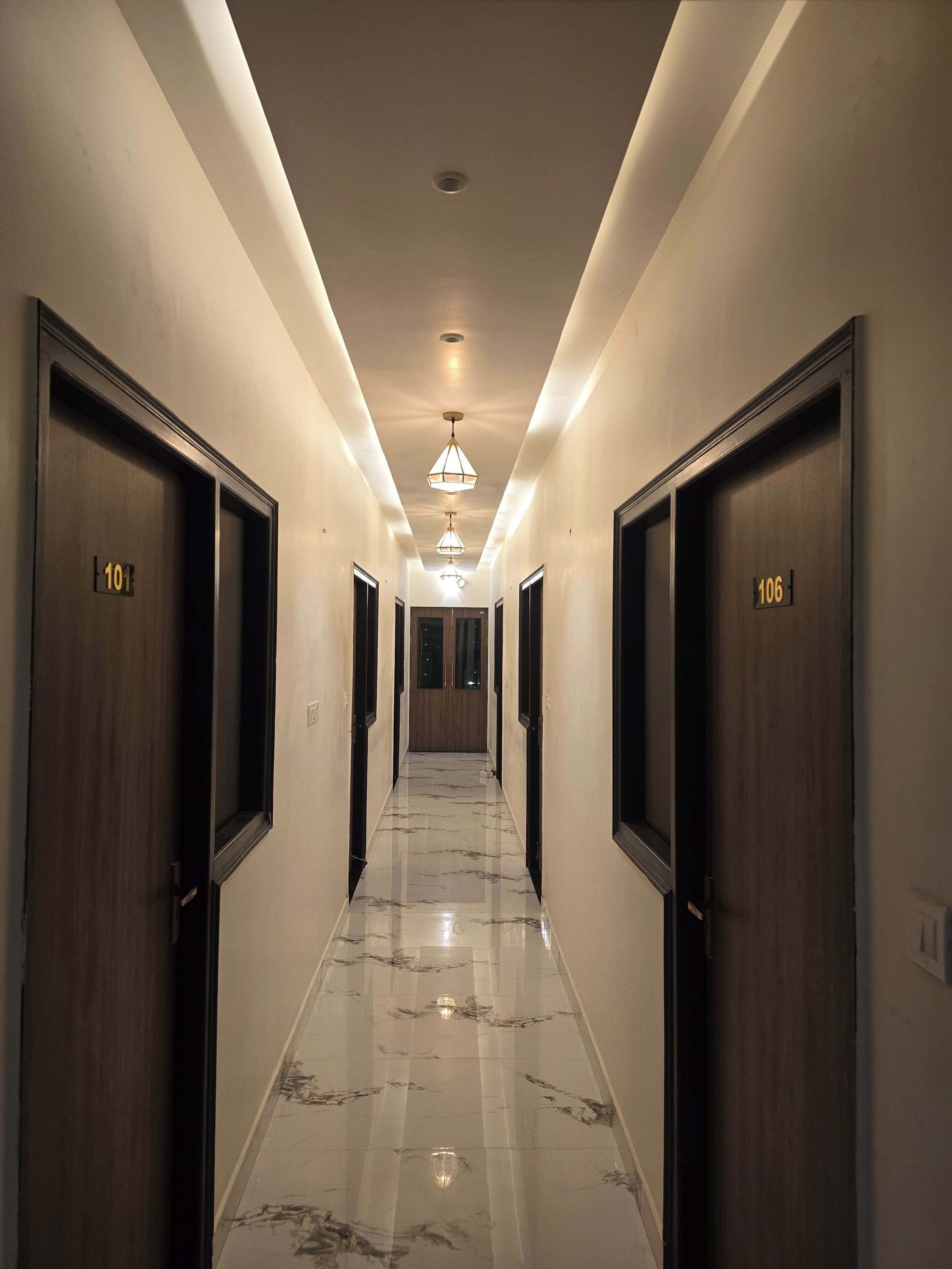 A hotel hallway with marble flooring, wooden doors numbered 101 and 106, and pendant lighting.