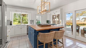 Una cocina moderna con armarios blancos, una isla azul y taburetes de mimbre.