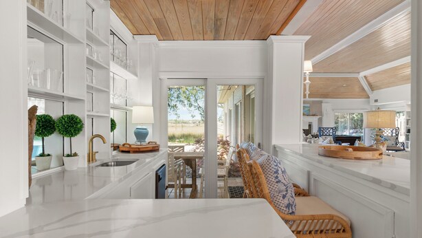 Una cocina moderna con armarios blancos, encimera de mármol y techo de madera.