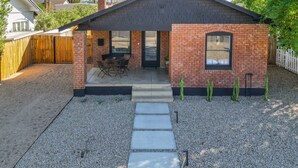 A small brick house with a patio, a covered outdoor seating area, and a gravel driveway.