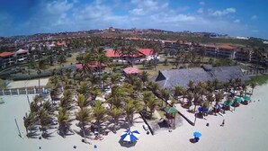 A coastal resort with a beach, palm trees, and a cluster of buildings with red roofs.