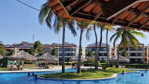 A swimming pool area with palm trees, thatched umbrellas, and a poolside seating area.