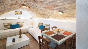 Une pièce chaleureuse avec un plafond en pierre, un canapé blanc agrémenté de coussins à motifs, une table à manger en bois avec des chaises, et une petite table basse blanche.