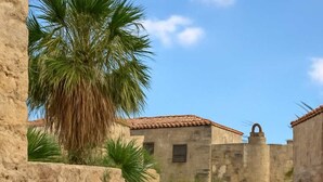 A narrow cobblestone pathway flanked by stone walls, leading to a building with a red door. - Menexes Suites Fiorelli Suite with Garden View (Monemvasia)