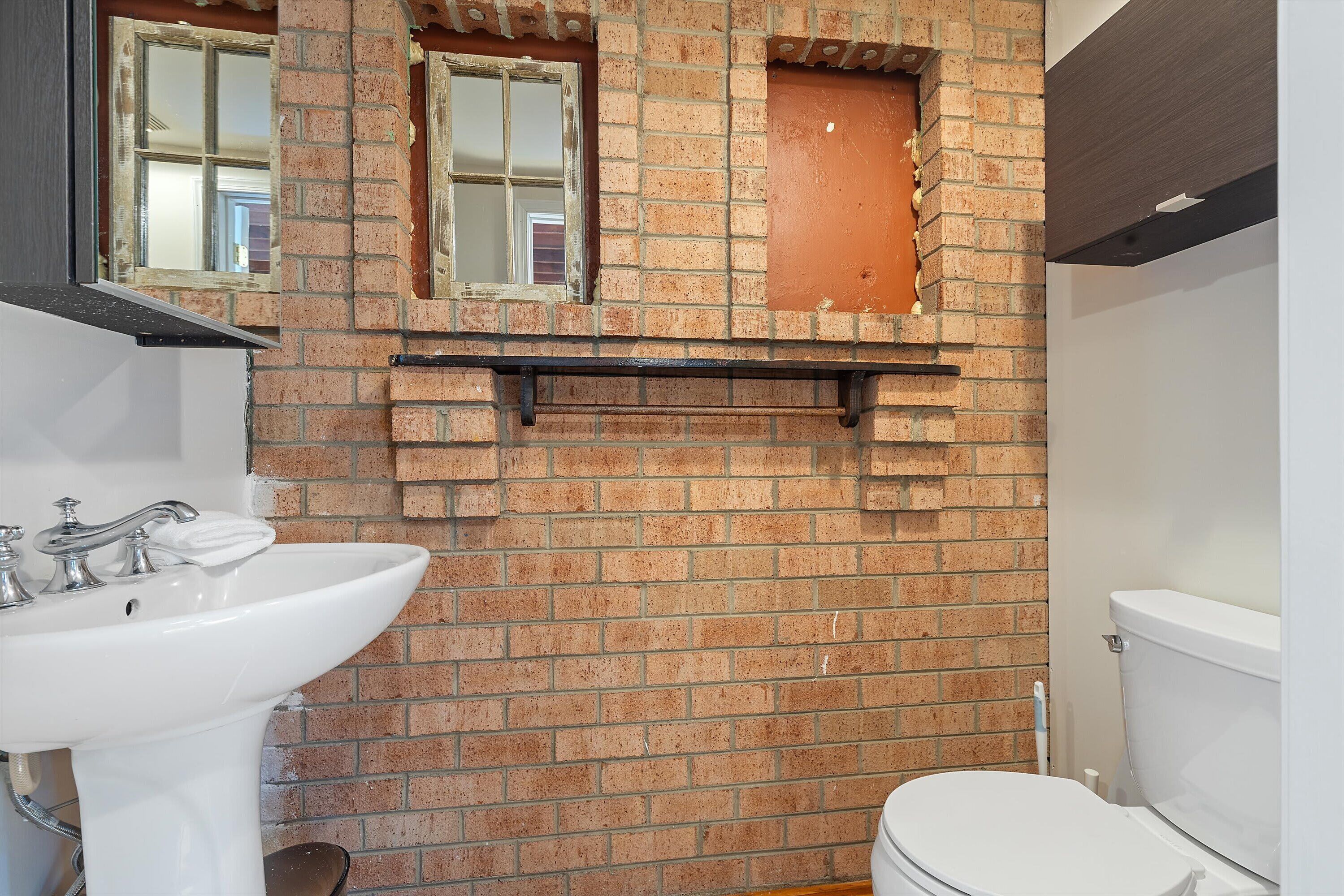 A bathroom with a white sink, a toilet, and a brick wall.