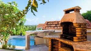 An outdoor brick oven with a view of a swimming pool and greenery. - Villa Caryota | Mountain Panorama & 29ft (9m) Private Pool (le Marin)