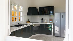 A kitchen with black cabinets, a stainless steel refrigerator, and a window with blinds. - Villa Caryota | Mountain Panorama & 29ft (9m) Private Pool (le Marin)